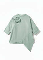 Bluză oversize verde pastel, cu croială amplă și tiv asimetric, fotografiată pe fundal neutru.