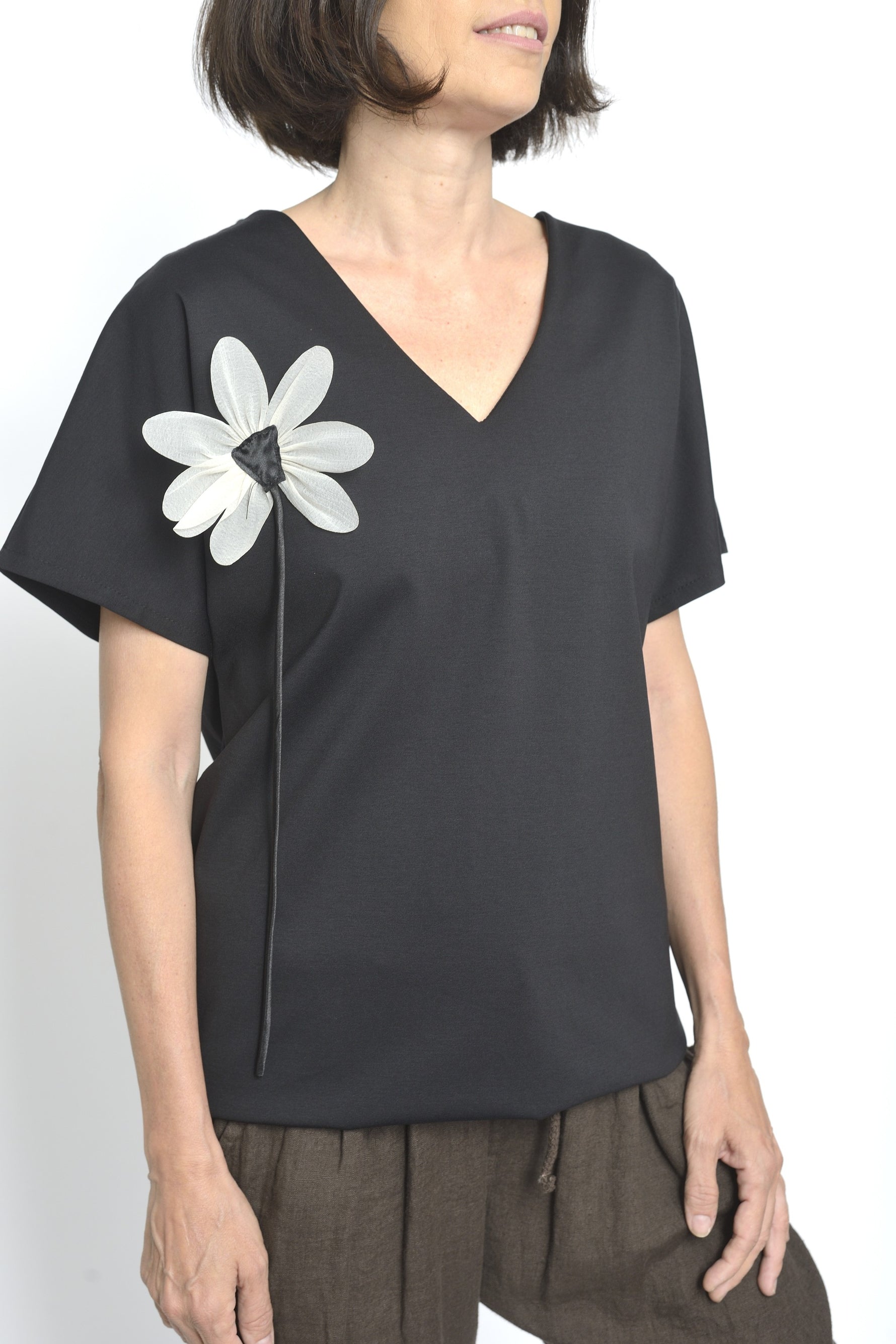 Bluza lungă neagră cu decolteu în V și floare albă decorativă aplicată pe umăr.