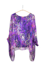 Bluză vaporoasă mov cu imprimeu abstract în tonuri de albastru, roz și alb, cu mâneci largi și tiv asimetric.