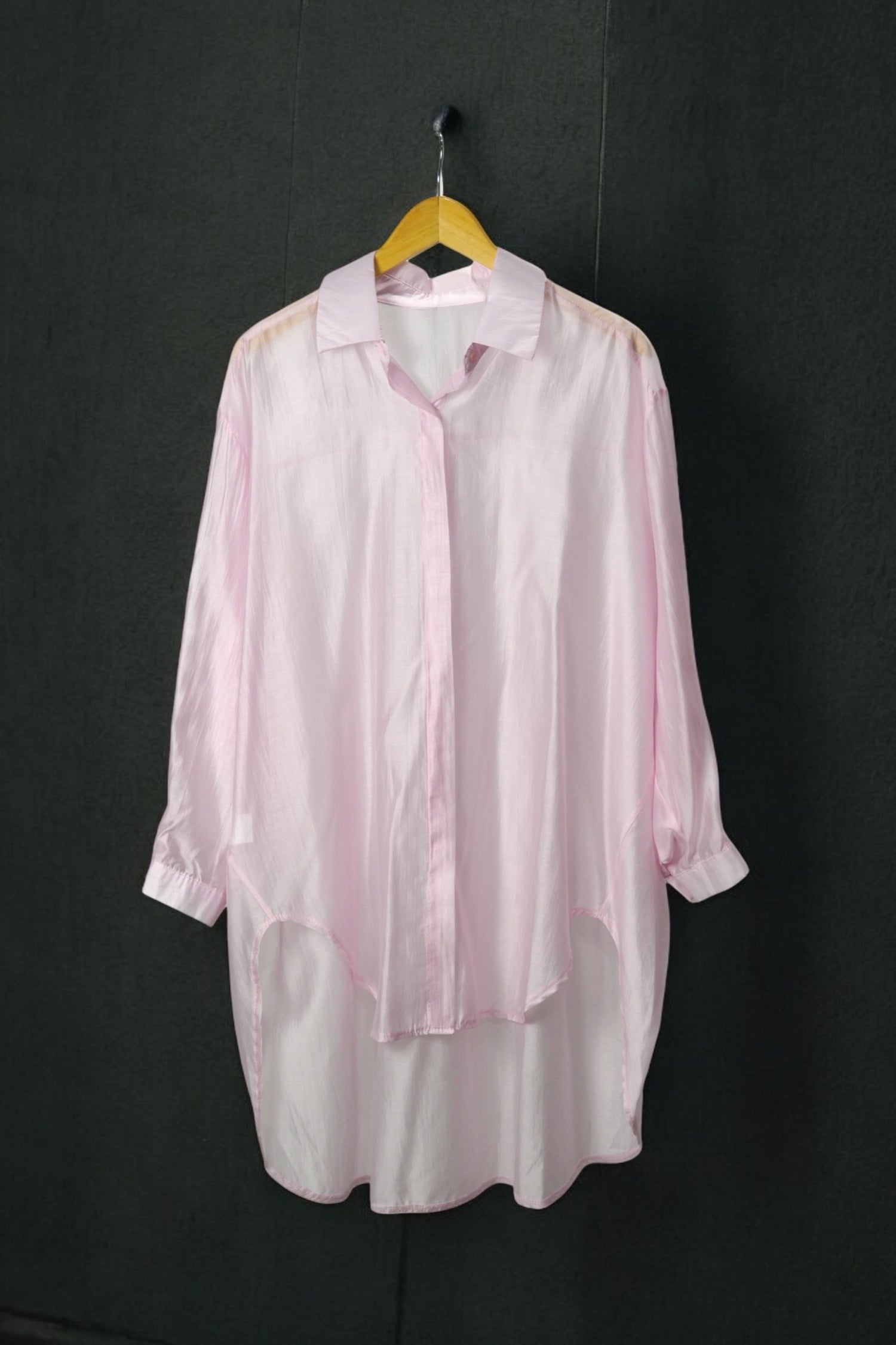 Cămașă oversized roz pastel, cu material ușor transparent, prezentată pe umeraș, fundal gri.