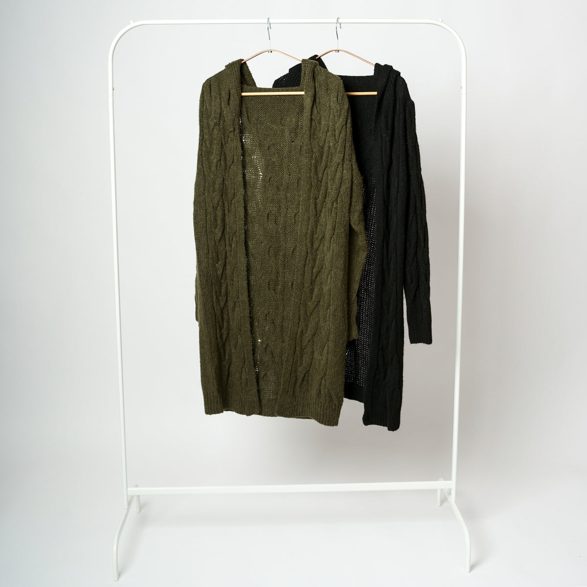 Cardigan lung tricotat cu glugă, disponibil în culorile kaki și negru, pe umerașe.