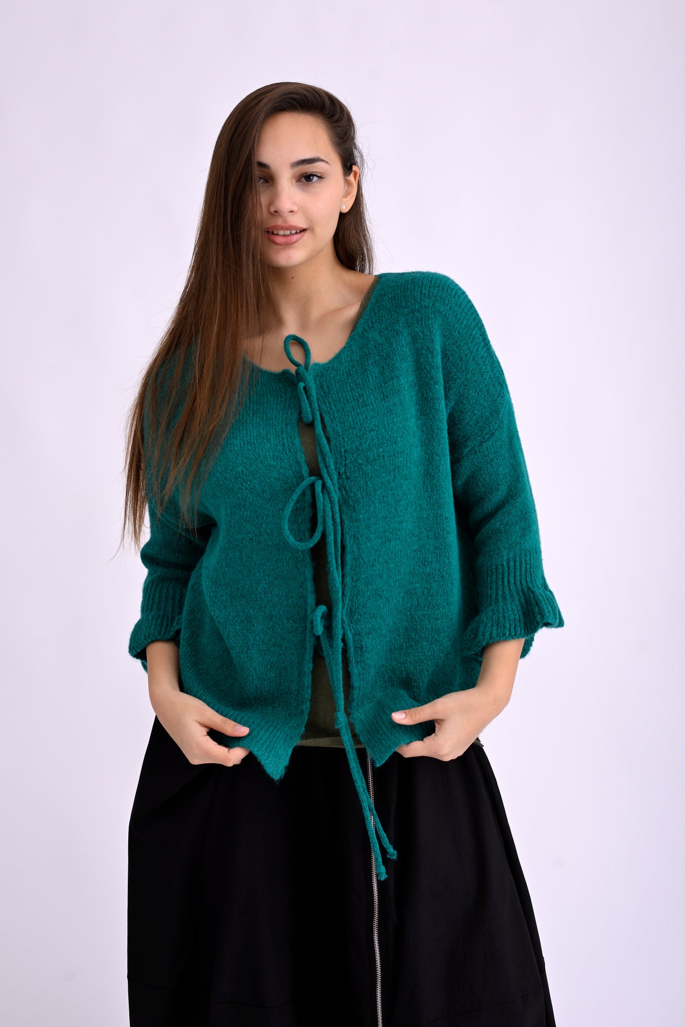 Model poartă cardigan tricotat verde, scurt, cu șnur și umeri căzuți, pe fundal alb.