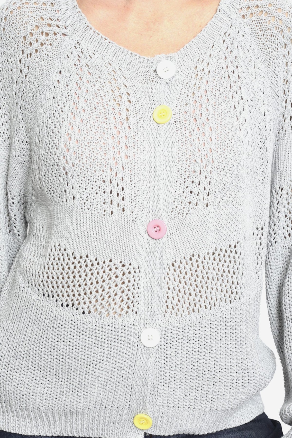 Detaliu al unui cardigan gri tricotat cu nasturi colorați și model perforat fin.