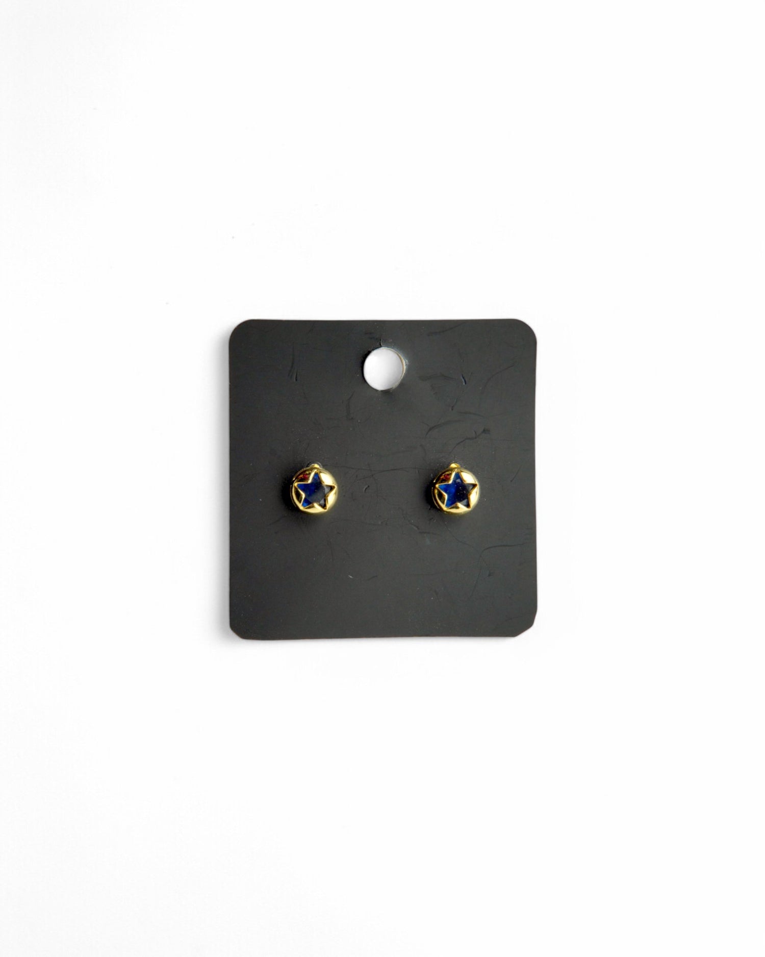 Cercei aurii cu steluță albastră, prezentați pe un card de bijuterii negru, cu fundal alb.