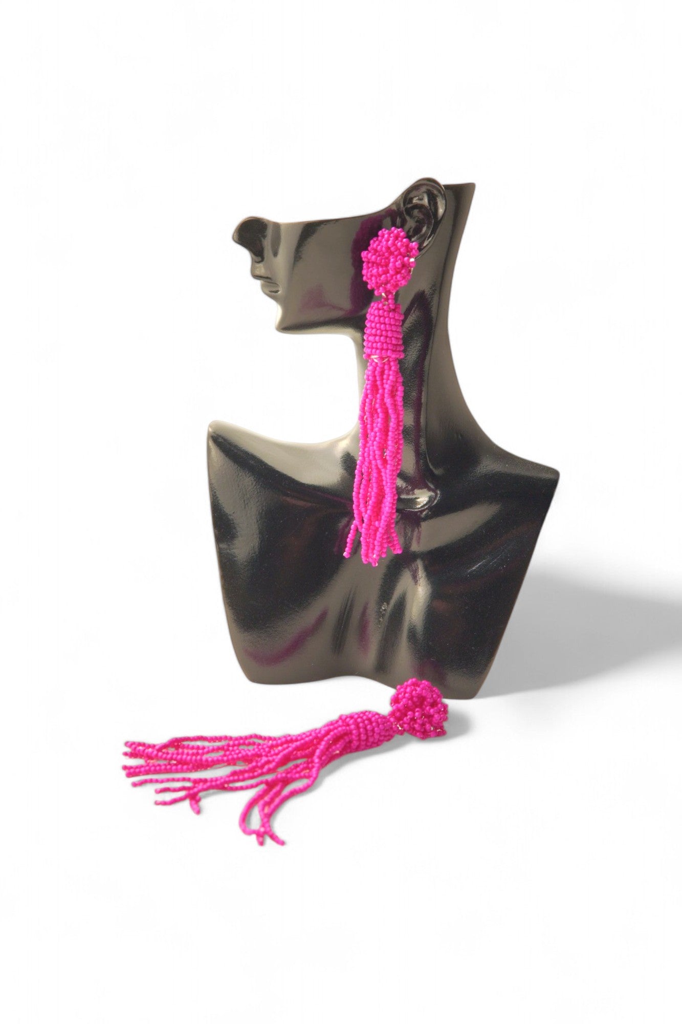 Cercei lungi, tip ciucuri, realizați din mărgeluțe roz, prezentati pe suport de expunere.