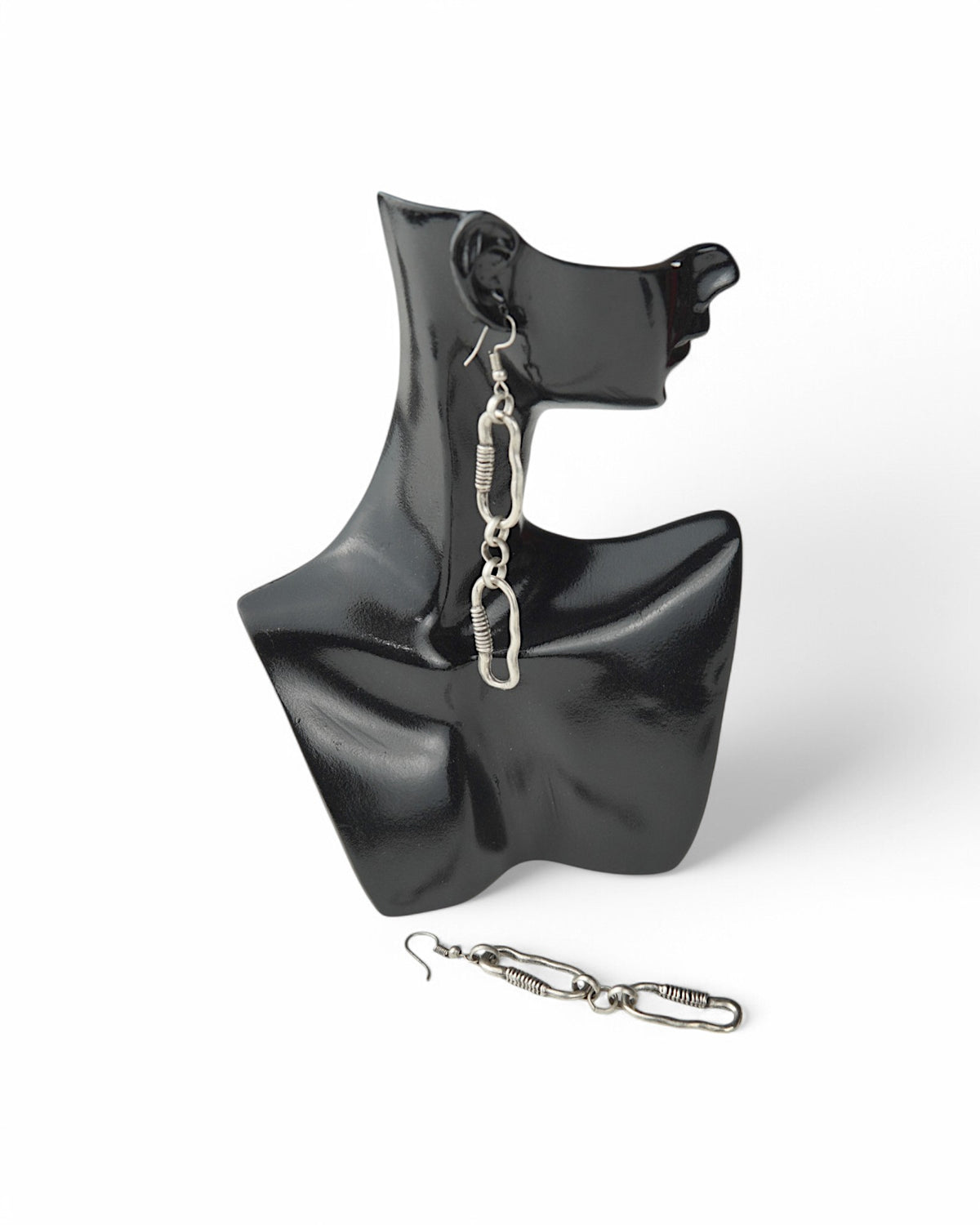 Cercei cu două verigi neuniforme, prezentați pe un suport de afișare negru