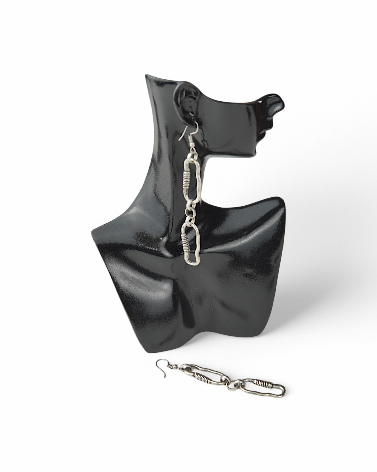 Cercei cu două verigi neuniforme, prezentați pe un suport de afișare negru