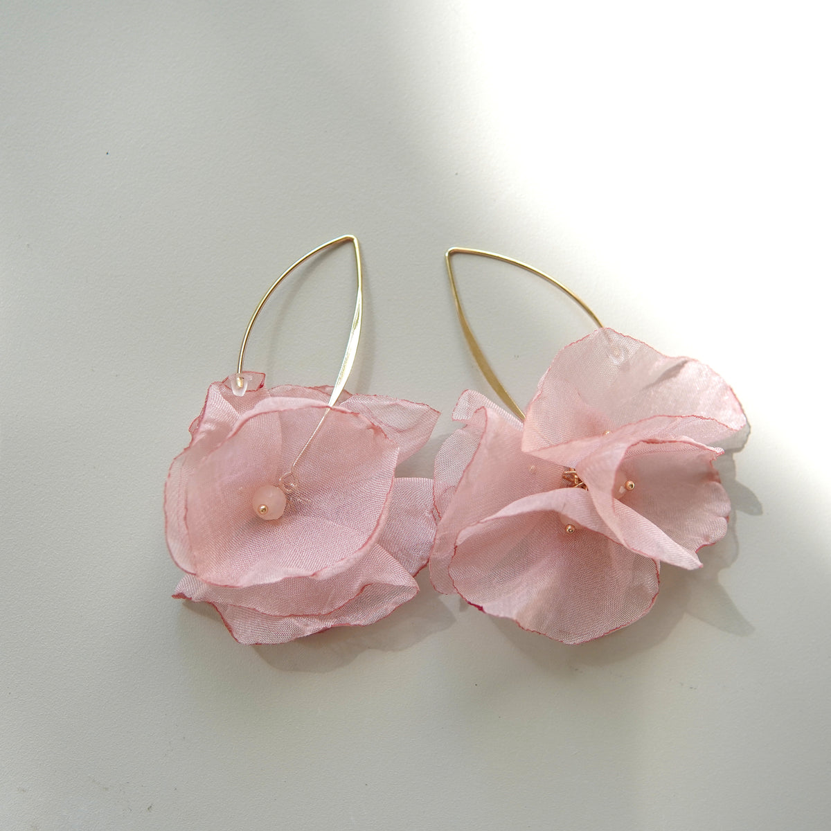 Cercei lungi din oțel inoxidabil cu flori satinate roz pastel și perlă decorativă centrală.