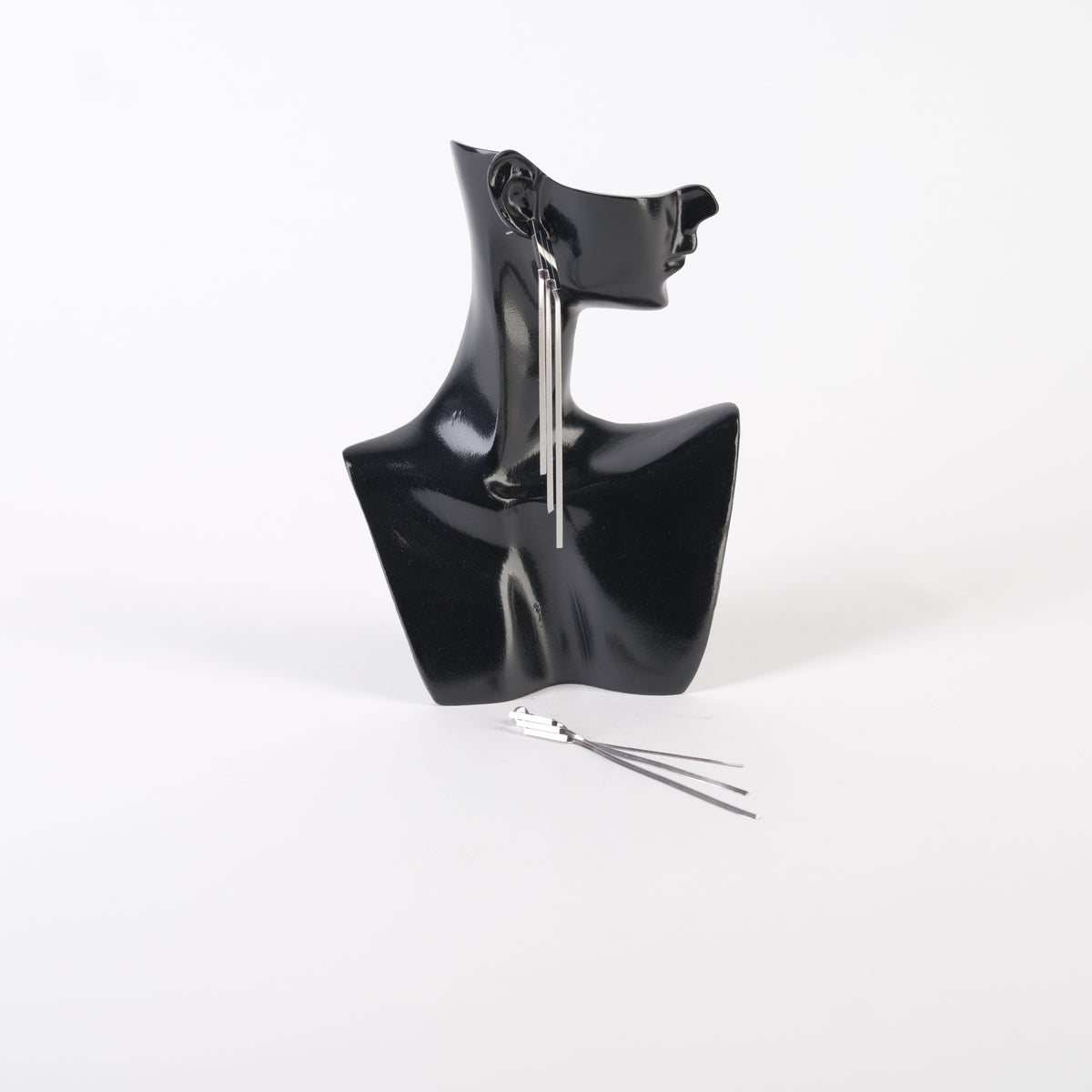 Cercei lungi din oțel inoxidabil, cu bloc rigid în partea superioară și franjuri metalici flexibili, finisaj argintiu, prezentați pe bust manechin negru.