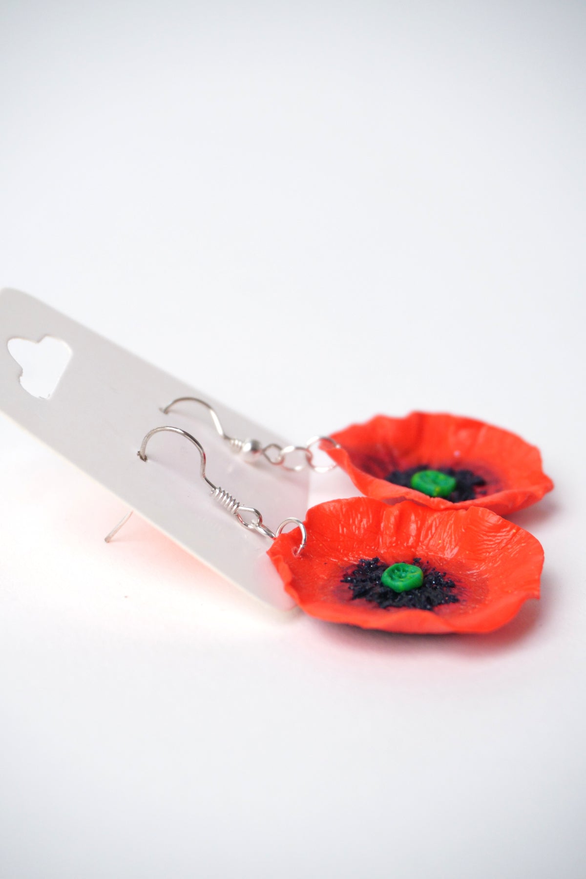 Cercei handmade cu flori de mac din fimo, priviți din lateral, cu cârlige metalice argintii.