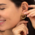 Cercei rotunzi din alamă reciclată, cu formă organică neregulată și finisaj auriu lucios, purtați la ureche.