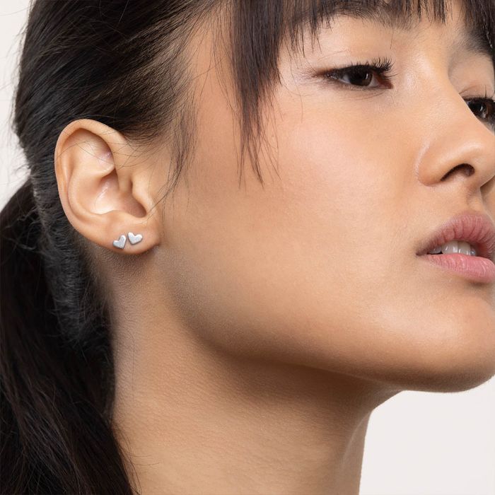 Model poartă cercei mici în formă de inimă, placate cu argint, de la Vestopazzo, cu un design discret și feminin.