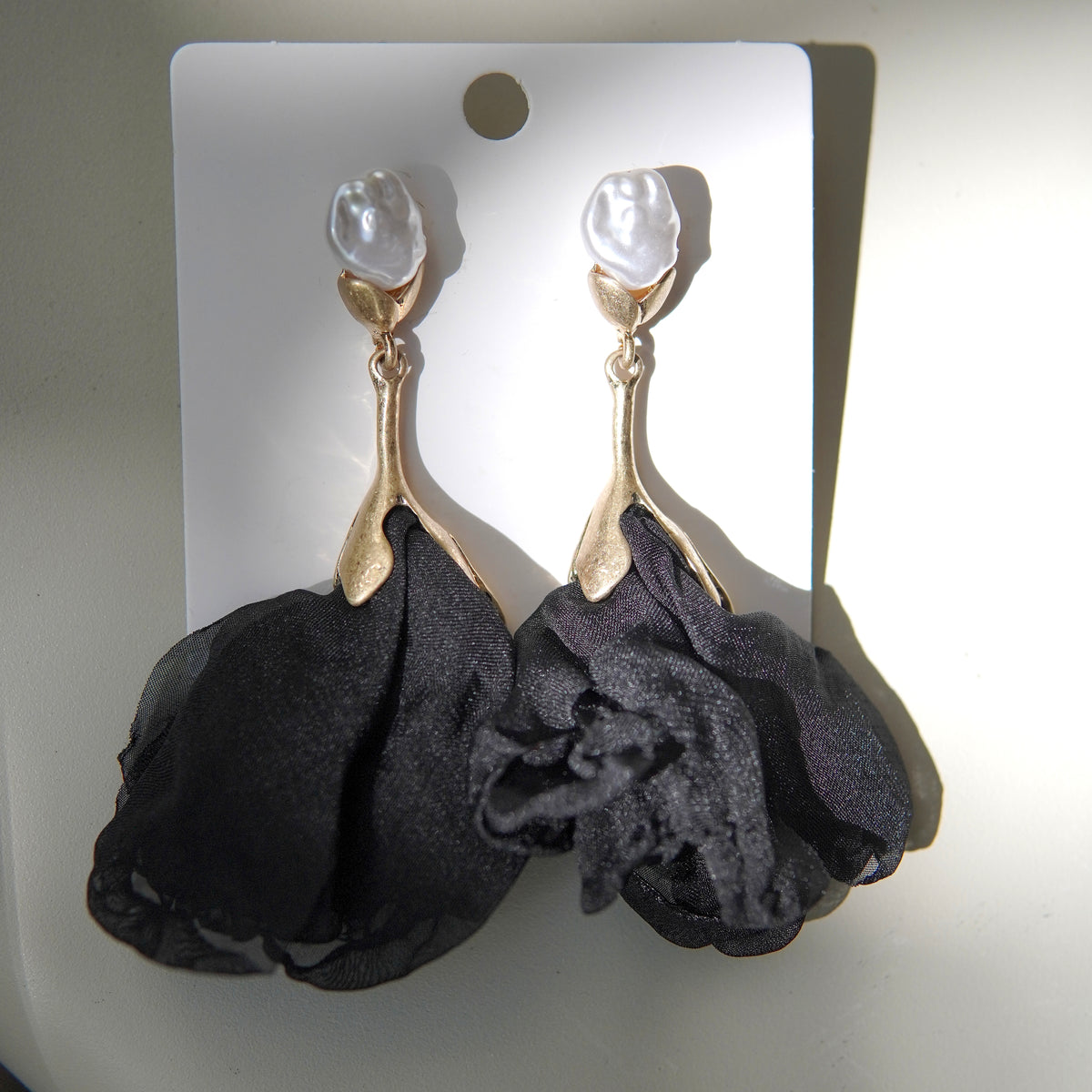 Vedere frontală a unei perechi de cercei cu perlă albă și floare din material satinat negru.
