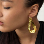 Cercei din alamă model panglică neregulată, purtați de model; finisaj auriu mat, lungime 6,5 cm, sistem de prindere cu șurub.