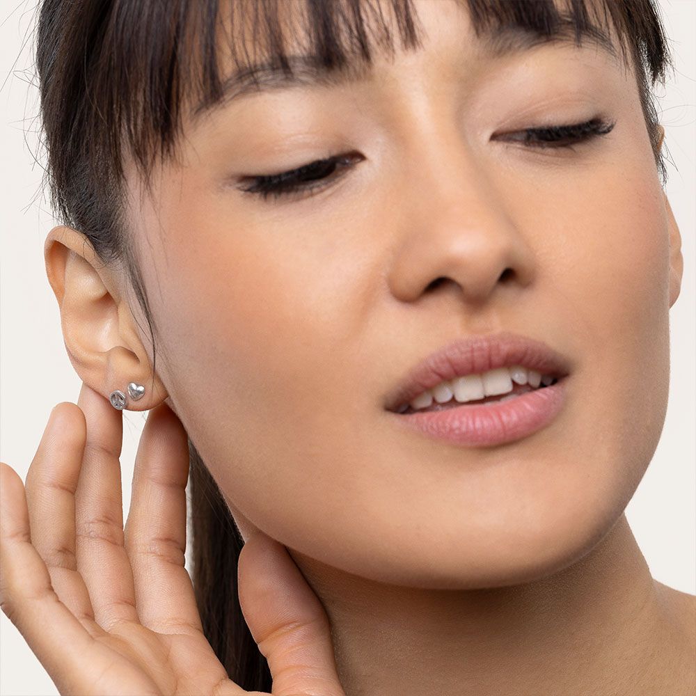 Cercei mici în formă de inimă și simbolul păcii, purtați în lobul urechii unei femei cu păr prins și breton