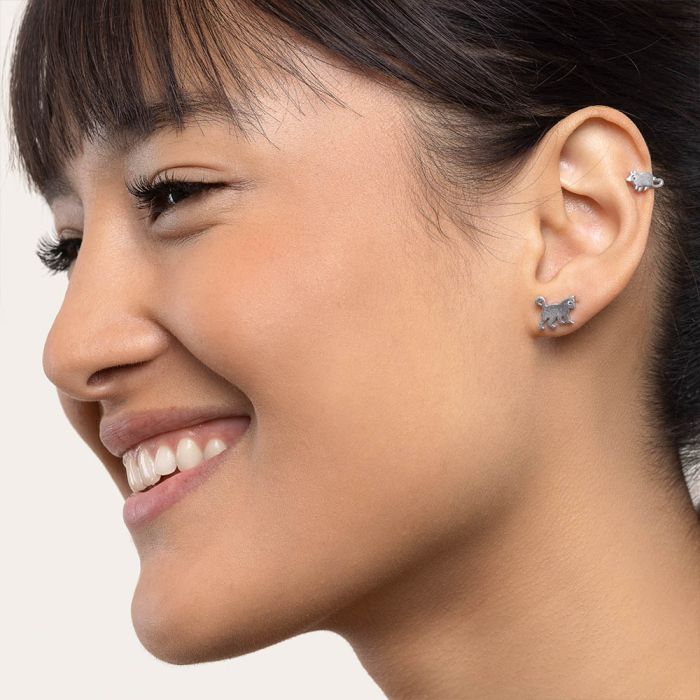 Cercei mici în formă de pisică și șoricel, purtați de o femeie care zâmbește, cu păr prins și breton