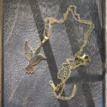 Colier cu pandantiv colibri din oțel inoxidabil auriu, prezentat pe fundal din lemn.