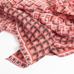 Prim-plan cu materialul unei eșarfe corai din bumbac și mătase, cu margini cusute și imprimeu geometric repetitiv.