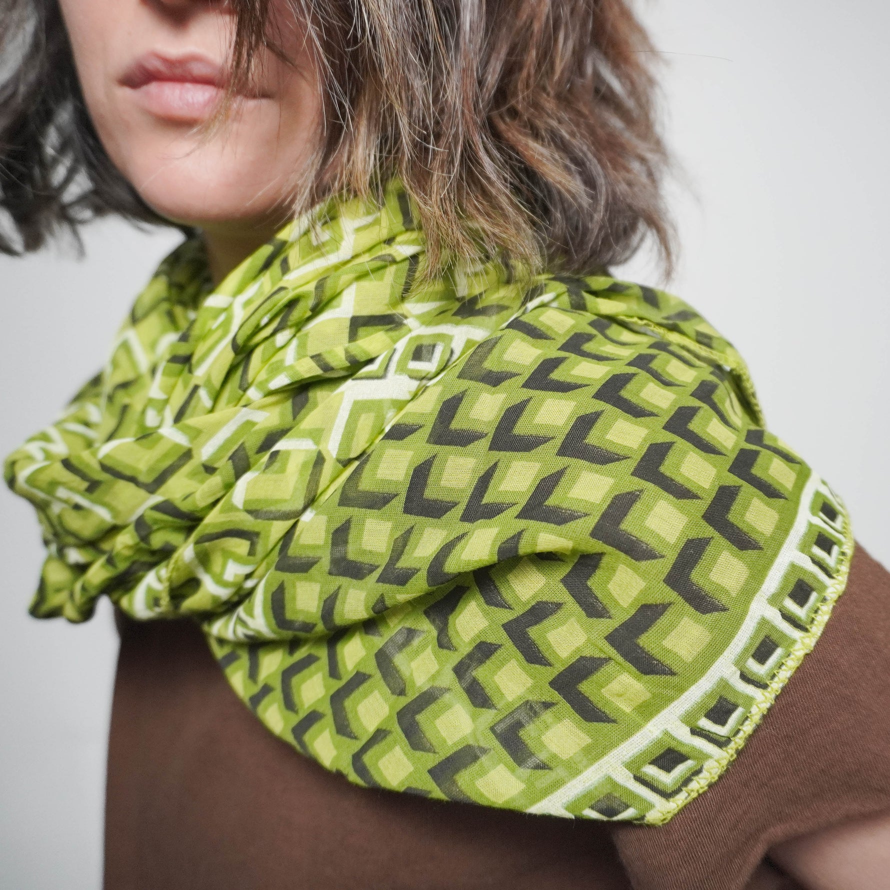 Eșarfă ușoară din bumbac și mătase în tonuri de verde cu imprimeu geometric, purtată pe umeri peste o bluză maro.
