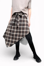 Fustă în carouri cu tiv asimetric, surprinsă în mișcare, evidențiind fluiditatea materialului și stratificarea.