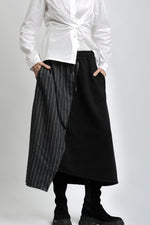 Fustă asimetrică din jerse negru cu panou cu imitație de jeans, purtată cu cămașă albă și bocanci.