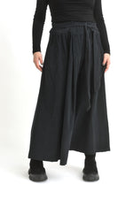 Fustă lungă neagră din catifea reiată, văzută din spate, cu talie elastică și plisare ușoară.