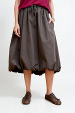 Fustă midi cu croială balon în maro închis, talie elastică cu șnur și buzunare laterale, vedere frontală pe fundal alb.