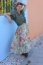 Fustă midi lejeră cu imprimeu floral pastelat, purtată cu o cămașă verde și ghete casual, într-un decor colorat.