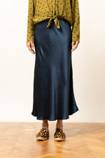 Detaliu frontal al unei fuste satinate albastru închis, lungime midi, cu cămașă verde cu buline.