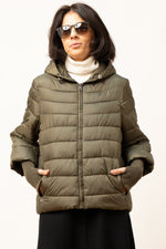 Prim-plan jachetă matlasată verde cu fermoar și buzunare laterale, purtată cu helancă albă.