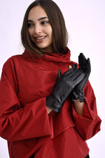 Mănuși negre din piele ecologică, purtate de o femeie îmbrăcată în roșu, cu design elegant și finisaj lucios.