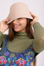 Pălărie tip clop din lână bej, cu bor moale și croială elegantă, purtată pe model.