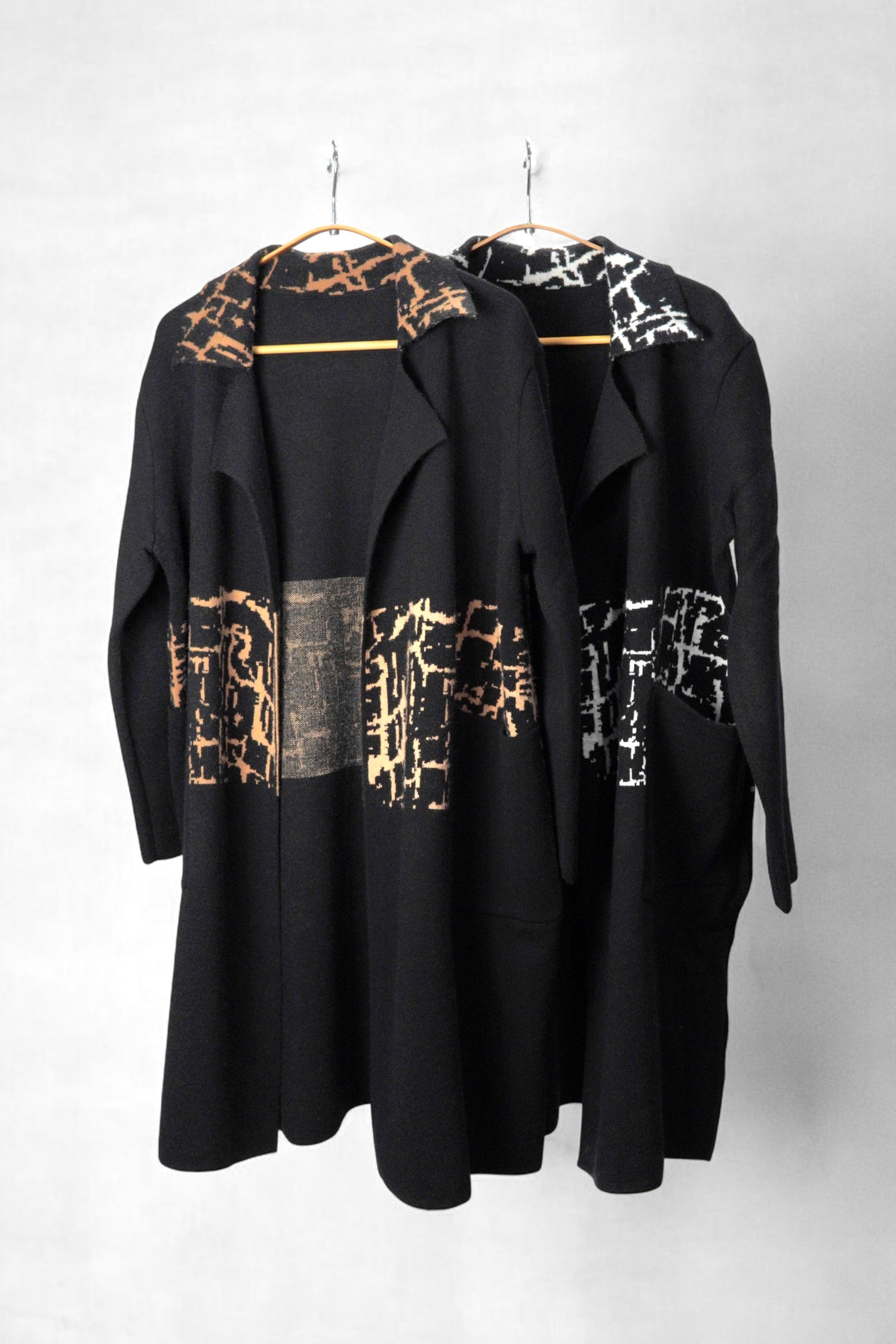 Paltoane negre cu imprimeuri contrastante în alb și maro, expuse pe umerașe pentru evidențierea modelelor.