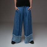 Pantaloni largi din denim albastru cu manșete evazate și tiv franjurat, purtați cu poncho croșetat colorat.