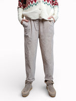 Model purtând pantaloni conici din catifea reiată crem, cu croială lejeră și talie elastică.