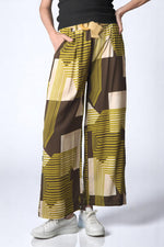 Pantaloni vaporoși cu imprimeu geometric în verde muștar și maro, fotografiați din față.