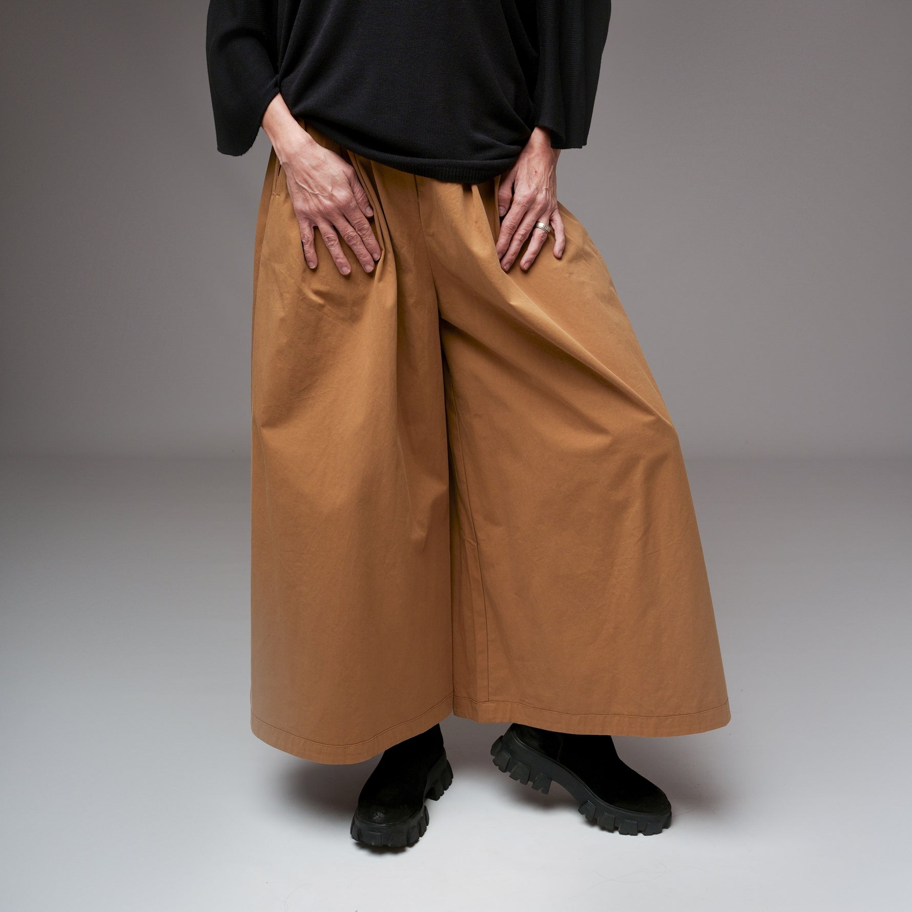 Model purtând pantaloni camel largi din bumbac structurat, cu top negru lejer, în studio cu fundal gri.
