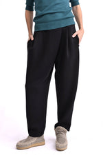 Pantaloni tip trening conici negri, cu pliuri la talie și croială lejeră, purtați pe model, vedere din față.