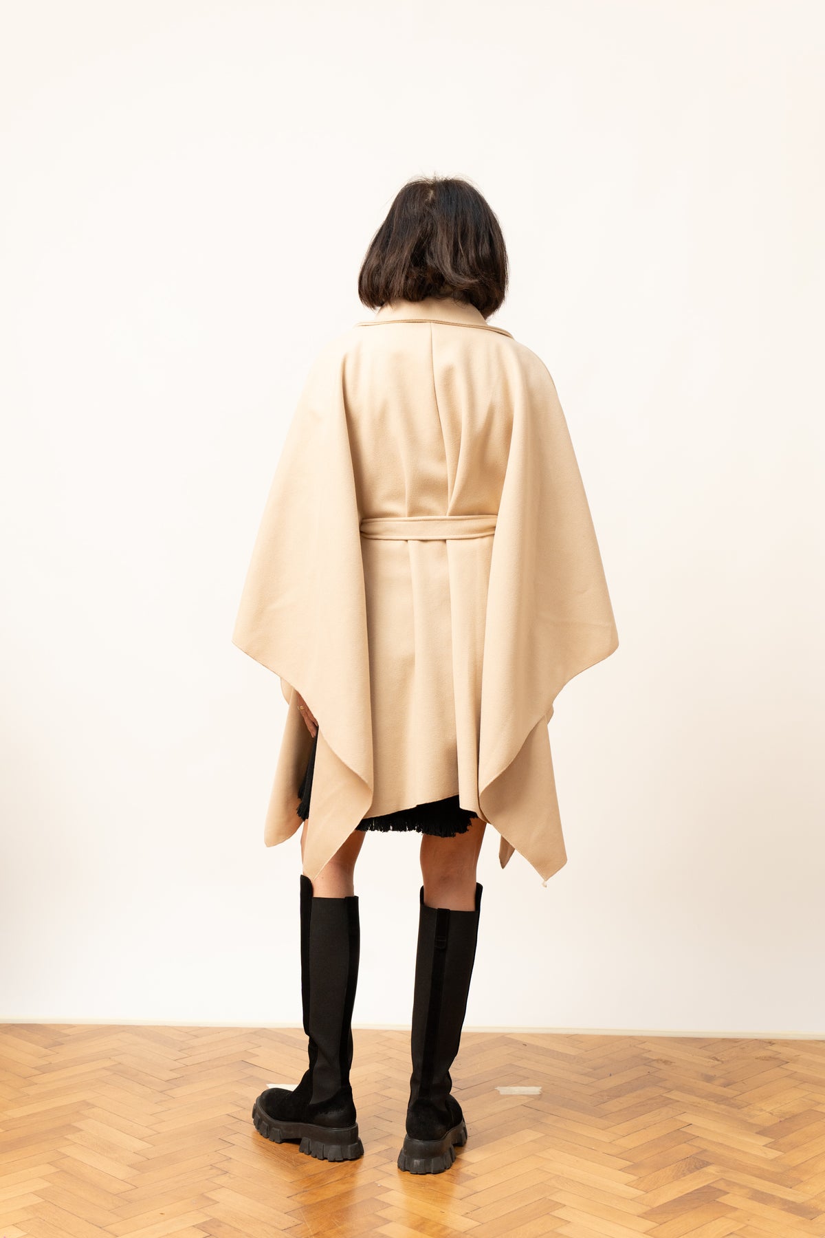 Pelerină bej cu cordon și croială amplă, vedere din spate pe model.