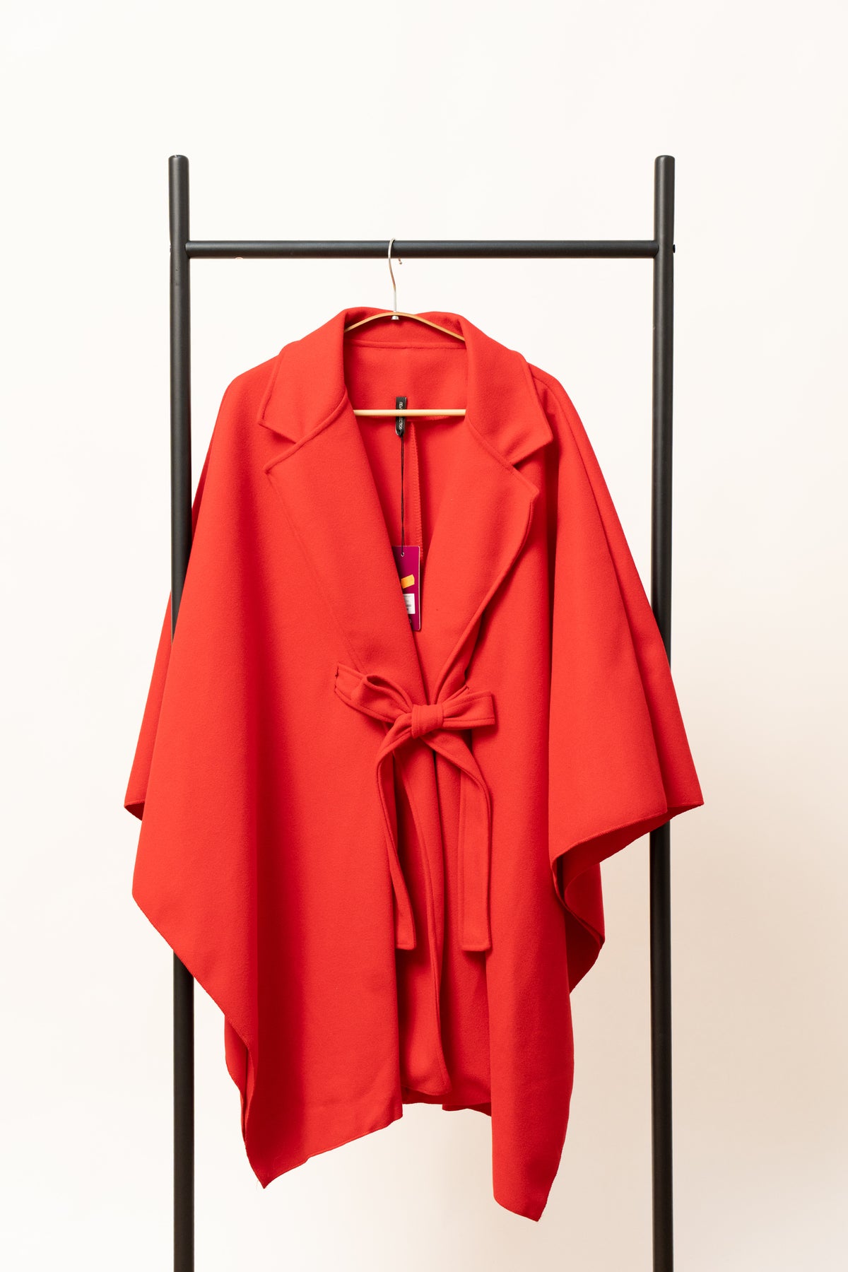 Pelerină roșie tip palton, cu cordon și revere, prezentată pe umeraș.
