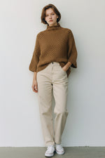 Pulover damă tricotat camel, purtat într-o ținută casual cu pantaloni deschiși la culoare.