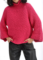 Detaliu mâneci largi și tricot solzișori la pulover roz cu umeri căzuți.