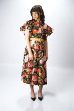 Variantă pe fundal negru cu imprimeu floral verde-oliv, cu volane ample la umeri și nasturi frontali.