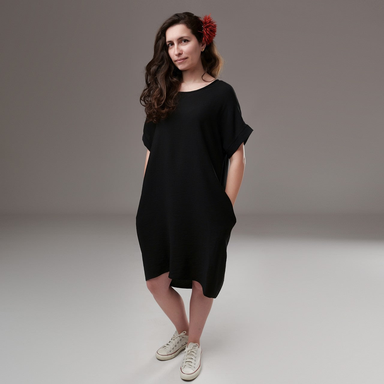 Rochie vaporoasă neagră cu guler rotund, lejeră și ușor asimetrică, accesorizată cu floare roșie