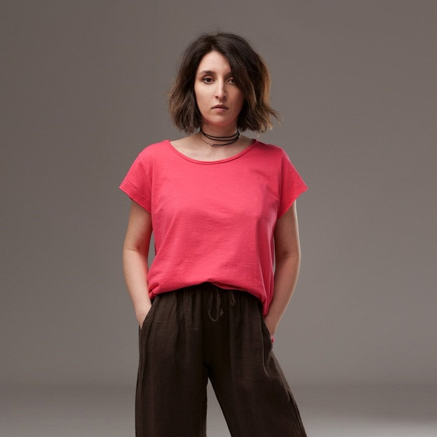 Tricou simplu din bumbac roz intens, cu guler rotund și mâneci scurte, purtat într-o ținută casual cu pantaloni maro largi.
