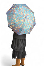 Umbrelă deschisă cu imprimeu floral inspirat din pictura „Migdal Înflorit” a lui Vincent van Gogh, în nuanțe de albastru și turcoaz.