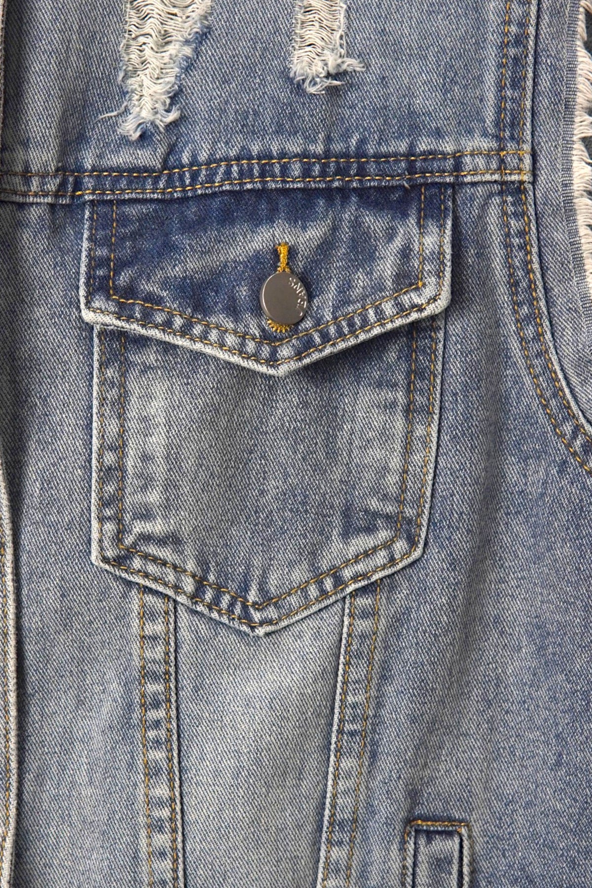 Buzunar frontal cu clapetă și nasture metalic al unei veste din denim albastru, cu cusături contrastante.