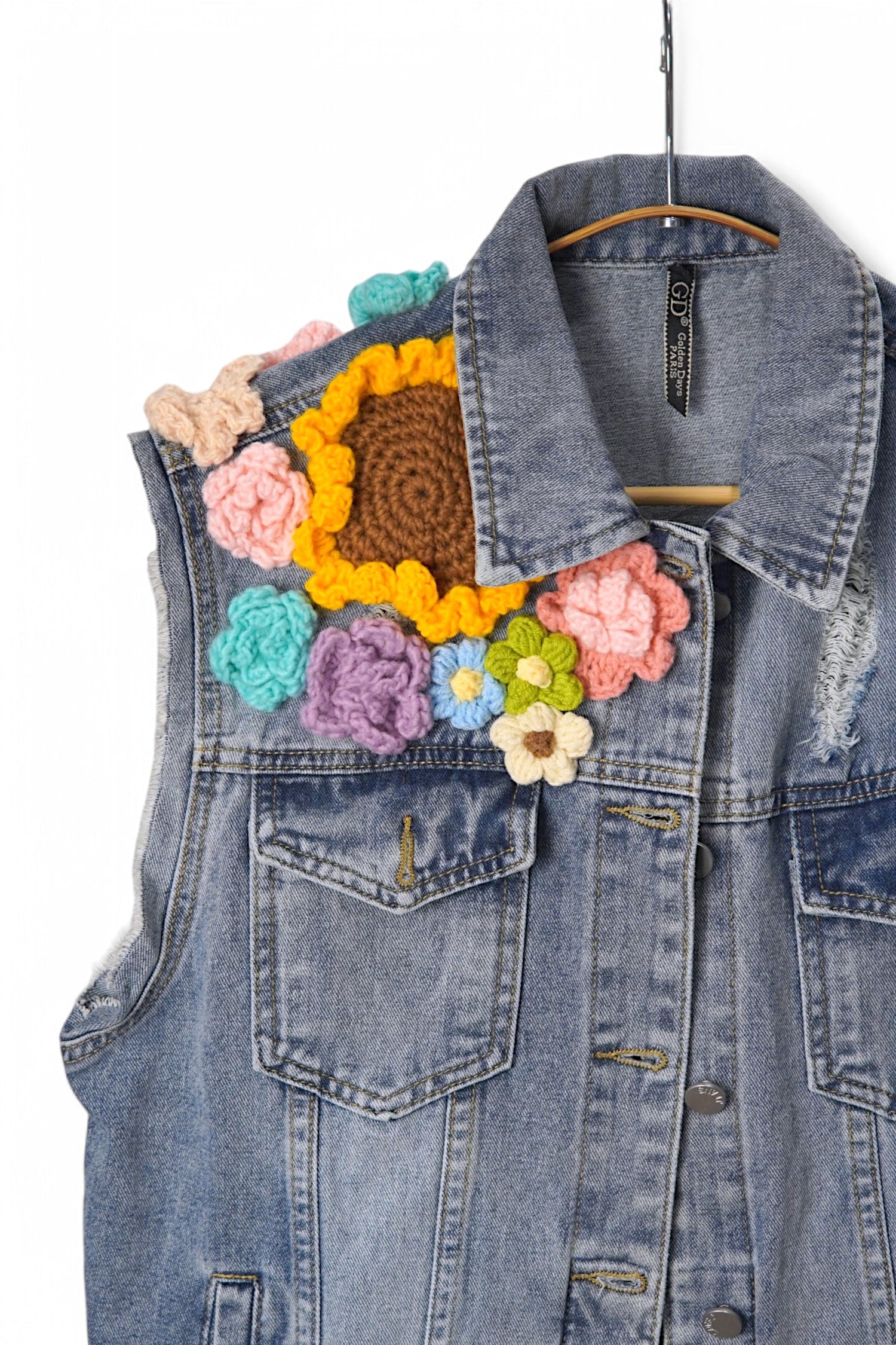 Vesta de jeans decorată cu aplicații croșetate colorate în formă de floare, poziționate pe umăr.