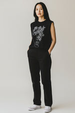 Vestă neagră cu broderie, purtată într-o ținută minimalistă, cu pantaloni negri și adidași albi.