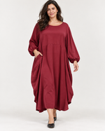 Rochie lungă satinată roșu închis, cu guler rotund și mâneci balon, purtată cu mâna în buzunar - All Above Boutique